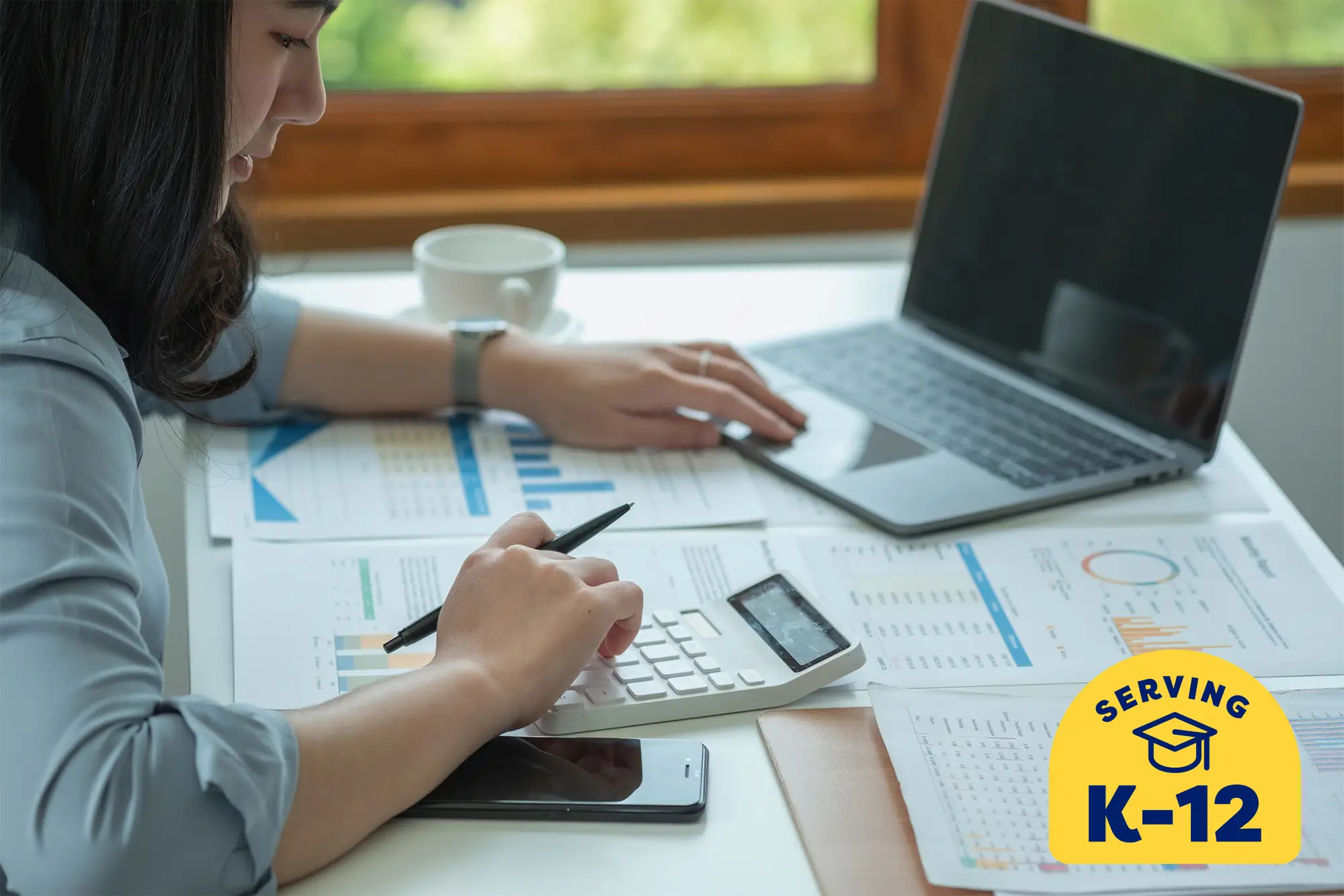 student at her desk using a laptop and calculator working on accounting class work