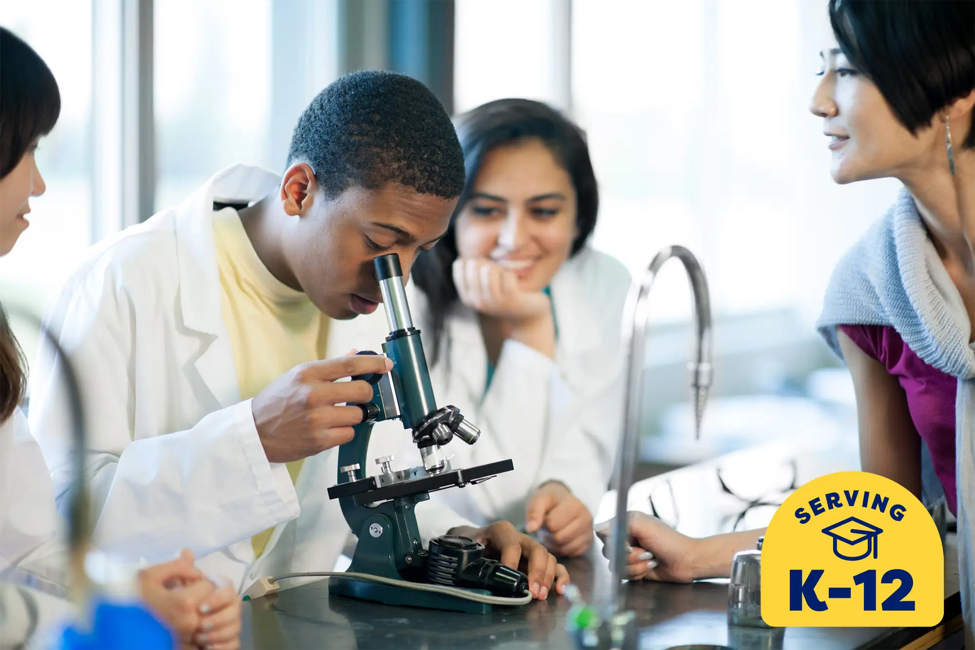 high school student wearing a lab coat and looking through a microscope